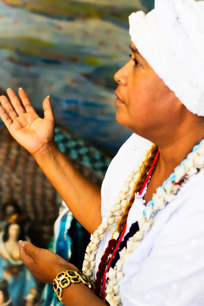 Mãe Iara de branco, com a mão erguida em oração
